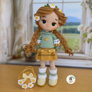 May include: A handmade crochet doll with long brown braids, adorned with white daisy accents. The doll wears a green sweater, yellow skirt, and white boots. A matching yellow basket with daisy details sits beside the doll. The doll is approximately 10 inches tall.