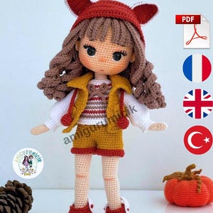 May include: A handmade crochet doll with brown curly hair, wearing a red fox-eared hat, a yellow vest, shorts, and red shoes. The doll has a detailed face and is standing next to a small orange pumpkin. The doll is a whimsical, handcrafted item.