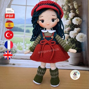 Op de afbeelding: Een handgemaakte gehaakte pop met een rode jurk, groen en rood gestreept shirt met lange mouwen en groene laarzen. De pop heeft donkerblauw haar, een rode hoed en een witte kraag. De pop is een handgemaakt item.