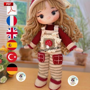 May include: A handmade crochet doll with long blonde hair, wearing a red and cream outfit. The doll has a red hat and overalls with a mushroom applique. The doll's eyes are large and black. The doll is standing in front of a window.