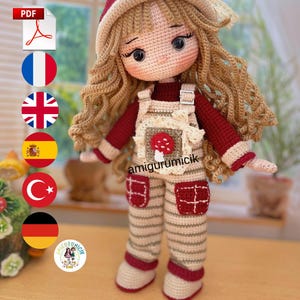 Puede incluir: Muñeca de ganchillo hecha a mano con pelo largo rubio, vestida con un conjunto rojo y beige. La muñeca tiene un sombrero rojo y un peto con un motivo de seta. El conjunto incluye pantalones a rayas y ribetes rojos. La muñeca mide unos 25 cm de altura.