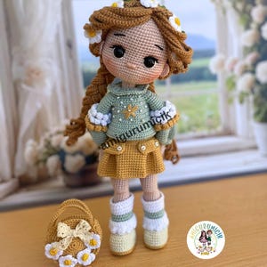 May include: A handmade crochet doll with brown hair adorned with a daisy crown. The doll wears a green sweater, yellow skirt, and white boots. A small basket with a bow and daisy accents sits beside the doll. The doll's name is "amigurumicik".
