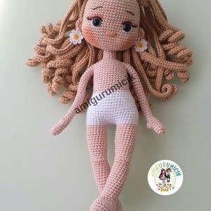 May include: A handmade crochet doll with light brown curly hair and a fair skin tone. The doll has a white diaper and small daisy earrings. The doll's arms and legs are extended. The doll is a handmade amigurumi.