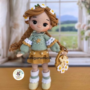 May include: A handmade crochet doll with brown hair adorned with white daisy flowers. The doll wears a green sweater, a yellow skirt, and white boots. It holds a small purse with daisy accents. The doll is approximately 8 inches tall.