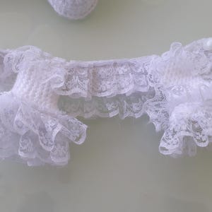 May include: White lace garter with ruffled edges. The garter is made of delicate lace and features a scalloped design. The garter is a bridal accessory.