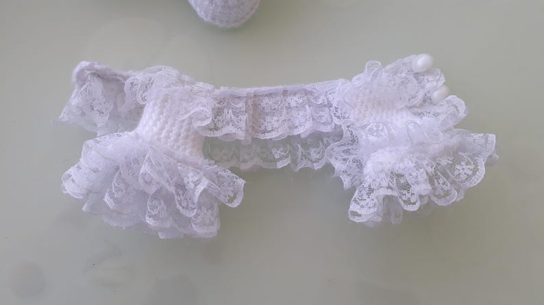 May include: White lace garter with ruffled edges. The garter is made of delicate lace and features a scalloped design. The garter is a bridal accessory.