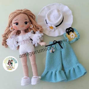 May include: A handmade crochet doll with long blonde hair, wearing a white dress with lace trim and white shoes. Accessories include a white hat, blue pants, and a small purse, all adorned with daisy accents. The doll is approximately 10 inches tall.