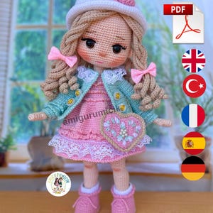 May include: A handmade crochet doll with blonde curly hair, wearing a pink dress, a blue jacket, and a white hat with a pink flower. The doll has a heart-shaped purse and pink shoes. The doll is a PDF pattern.