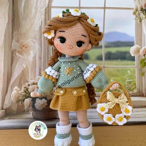May include: A handmade crochet doll with brown hair adorned with a daisy crown. The doll wears a green sweater, mustard skirt, and white boots. A matching purse with daisy accents completes the ensemble. The doll is holding a small purse.