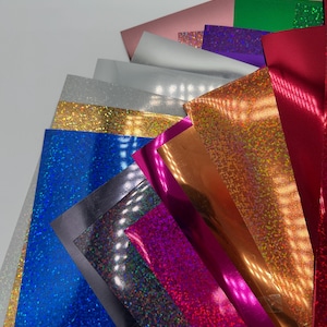 以下が含まれることがあります： 青、銀、金、ピンク、赤など、さまざまな色合いのカラフルなクラフト紙のコレクション。光を反射するキラキラまたはホログラフィック仕上げのシートもあります。紙は扇形に配置されています。