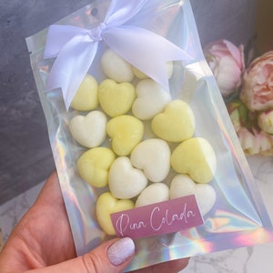 May include: A clear plastic bag with a white bow tied at the top. The bag contains a variety of heart-shaped wax melts in white and yellow. The bag has a pink label that says "Pina Colada".
