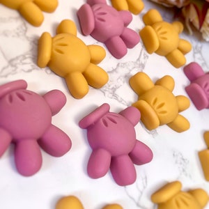 Könnte beinhalten: Eine Sammlung kleiner, handförmiger Silikonformen in Gelb und Rosa. Die Formen sind wie eine Hand mit vier Fingern und einem Daumen geformt.