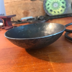 May include: A small, hammered metal bowl with a dark gray finish. The bowl has a slightly irregular rim and a textured surface.