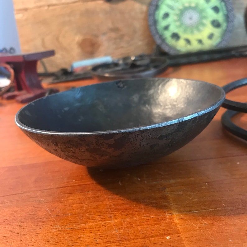 May include: A small, hammered metal bowl with a dark gray finish. The bowl has a slightly irregular rim and a textured surface.