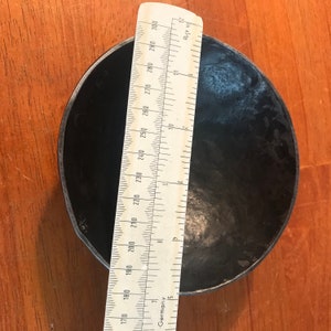 May include: A black metal bowl with a diameter of approximately 8 inches. The bowl is sitting on a wooden surface.