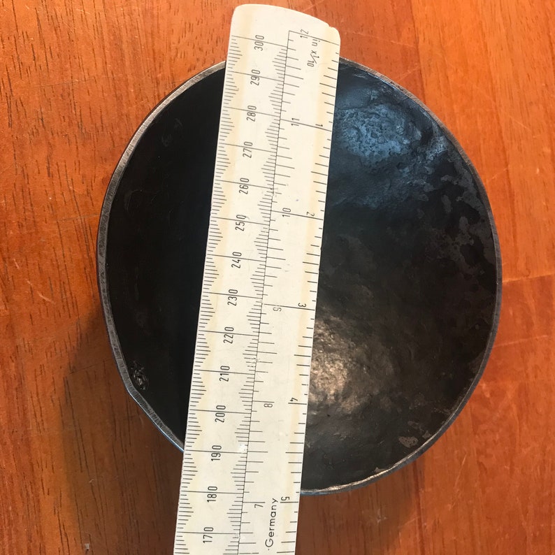 May include: A black metal bowl with a diameter of approximately 8 inches. The bowl is sitting on a wooden surface.