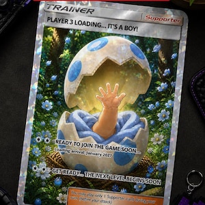 May include: A personalised trading card design with the text "THE BEST GAMER PREGNANCY REVEAL." The card features an illustration of a baby's arm emerging from a cracked egg, with the text "PLAYER 3 LOADING... IT'S A BOY!" and "READY TO JOIN THE GAME SOON..."