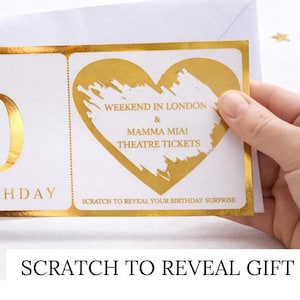 May include: A white birthday scratch-off card with gold foil accents. The card features a heart-shaped design with the text "Weekend in London & Mamma Mia! Theatre Tickets." The bottom reads "Scratch to reveal your birthday surprise."