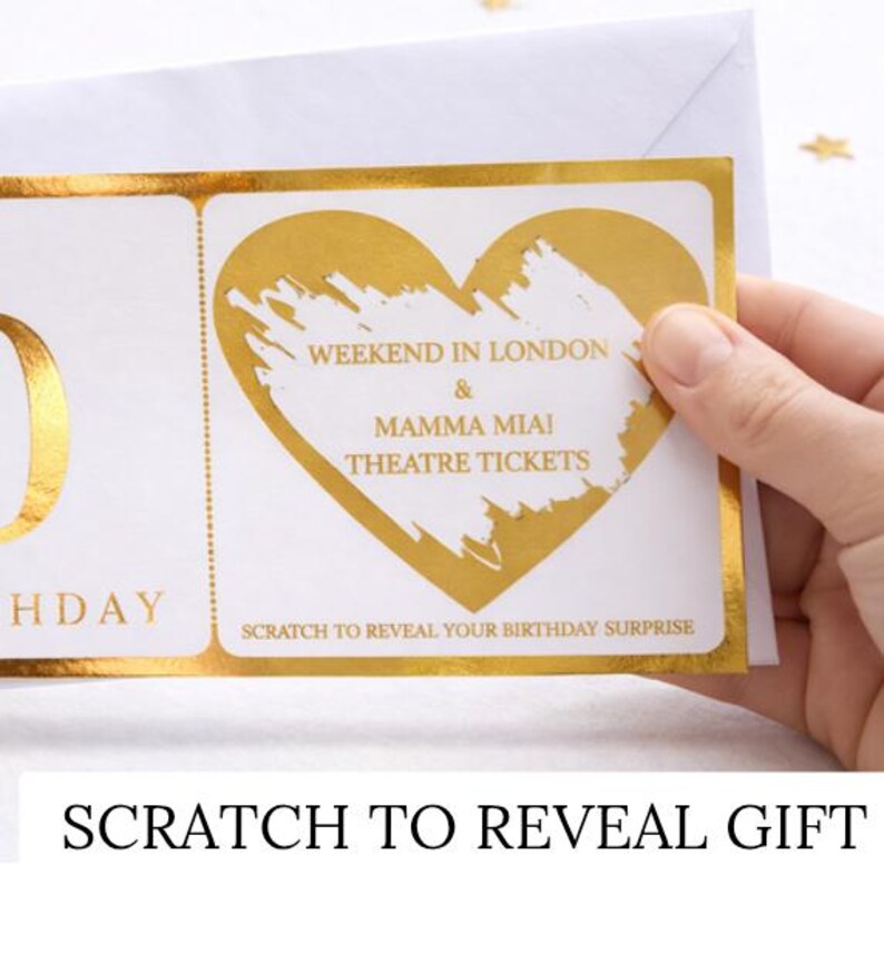 May include: A white birthday scratch-off card with gold foil accents. The card features a heart-shaped design with the text "Weekend in London & Mamma Mia! Theatre Tickets." The bottom reads "Scratch to reveal your birthday surprise."