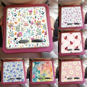 May include: Six different designs of square-shaped phone cases with floral patterns. The cases are pink, white, and blue with various floral designs, including daisies, ladybugs, and a bunny rabbit.