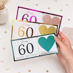May include: Three birthday cards with a white background, each featuring the number 60 in a different color: pink, gold, and dark green. The cards have a heart-shaped scratch-off area and the word "Mum" in cursive.