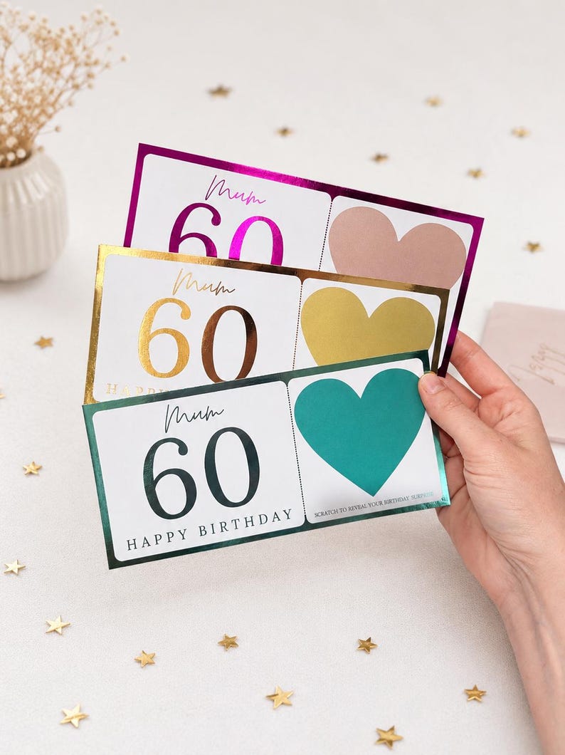 May include: Three birthday cards with a white background, each featuring the number 60 in a different color: pink, gold, and dark green. The cards have a heart-shaped scratch-off area and the word "Mum" in cursive.