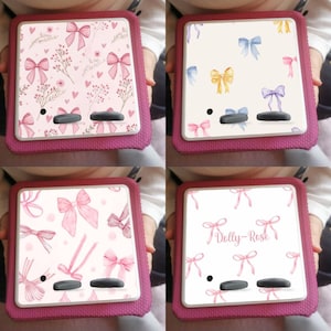 May include: Four pink e-reader covers with different bow designs. One cover has a pink floral pattern with bows, another has blue, yellow, and purple bows, a third has pink bows, and the last has pink bows with the text "Dolly-Rose".