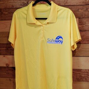 Puede incluir: Una camisa polo amarilla con un logotipo azul que dice "Safeway Transportation Services Corp."