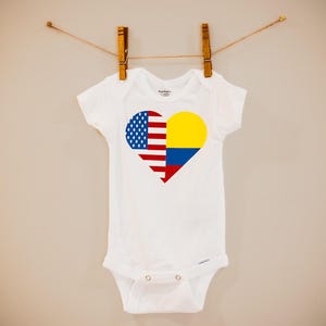 May include: White baby onesie with a heart-shaped design featuring the American and Colombian flags.