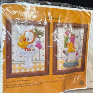 May include: A craft kit featuring two framed embroidery pieces with a bathroom theme. Each piece depicts a yellow duckling. One is at a sink, the other in a bathtub. The finished size is 5" x 7" (12.7cm x 17.7cm).
