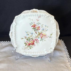 May include: A white porcelain plate with a floral design. The plate has a scalloped edge and is decorated with pink, red, and blue flowers.