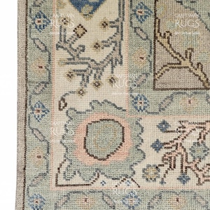May include: Detail of a patterned rug with a mix of light blue, cream, and pink colours. The design incorporates floral and geometric patterns, with a fringed border. The rug's texture is evident, indicating a woven construction. The rug is likely made of wool.