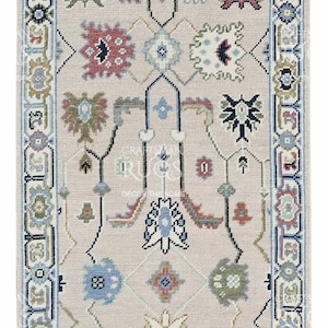 May include: Rectangular beige rug with an intricate pattern. The design features floral and geometric shapes in shades of blue, red, green, and black. The rug has a detailed border and a central medallion.
