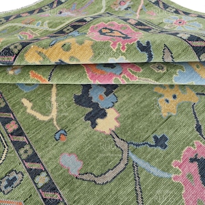 May include: A green rug with a floral pattern in shades of pink, blue, yellow, and cream. The rug has a dark blue border with a geometric design.