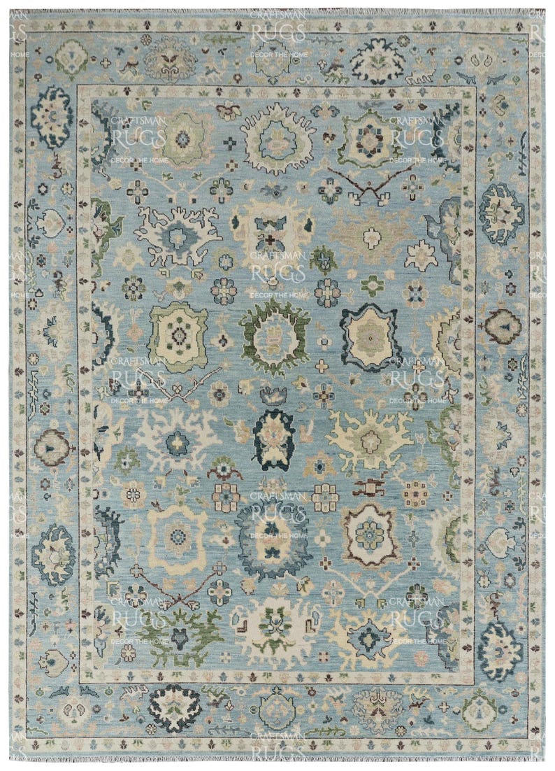 Pu&ograve; includere: Un tappeto rettangolare con sfondo azzurro e un intricato motivo floreale nei toni del crema, verde e blu navy. Il tappeto ha un bordo dettagliato e il testo "CRAFTSMAN RUGS DECOR THE HOME" &egrave; visibile.