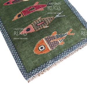 K&ouml;nnte beinhalten: Gr&uuml;ner rechteckiger Teppich mit Fischmuster in Rot-, Orange- und Blaut&ouml;nen. Der Teppich hat einen dunkelblauen und wei&szlig;en Rand. Der Text "CRAFTSMAN RUGS DECOR THE HOME" ist sichtbar.