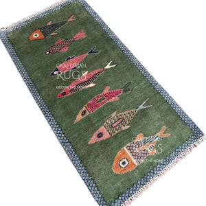 K&ouml;nnte beinhalten: Ein rechteckiger gr&uuml;ner Teppich mit einem sich wiederholenden Muster aus bunten Fischen. Die Fische sind in Rot-, Orange- und Schwarzt&ouml;nen gehalten und weisen aufwendige Designs auf. Der Teppich hat einen blauen Rand und den Text "Craftsman Rugs Decor the Home".