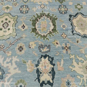 Pu&ograve; includere: Primo piano di un tappeto azzurro con un intricato motivo floreale. Il design presenta forme floreali e geometriche color crema, verdi e blu navy. Il tappeto ha un aspetto strutturato, che suggerisce una costruzione tessuta. L'estetica generale &egrave; tradizionale e decorativa.