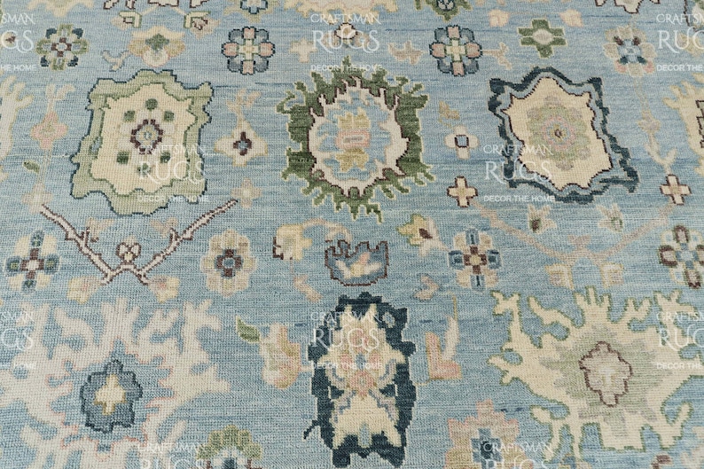 Pu&ograve; includere: Primo piano di un tappeto azzurro con un intricato motivo floreale. Il design presenta forme floreali e geometriche color crema, verdi e blu navy. Il tappeto ha un aspetto strutturato, che suggerisce una costruzione tessuta. L'estetica generale &egrave; tradizionale e decorativa.