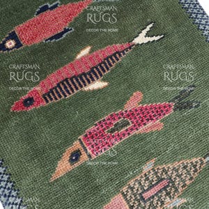 K&ouml;nnte beinhalten: Nahaufnahme eines gr&uuml;nen Teppichs mit einem sich wiederholenden Muster aus Fischen in Rot-, Rosa- und Schwarzt&ouml;nen. Die Fische sind stilisiert mit detaillierten Schuppen und Flossen. Der Teppich hat einen blau-wei&szlig;en Rand und den Text "CRAFTSMAN RUGS DECOR THE HOME".