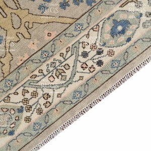 May include: Detail of a vintage rug with a floral pattern. The rug has a light blue border with floral motifs and a beige central field with intricate designs. The rug has a fringed edge. The measurements are in centimetres.