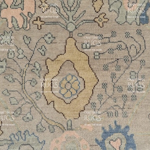 May include: Close-up of a beige rug with a detailed floral pattern. The design features a central yellow motif surrounded by blue, pink, and green floral elements. The rug has a vintage, distressed appearance.
