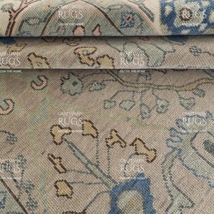 May include: Close-up of a section of a vintage rug with a detailed floral pattern. The rug features a muted colour palette of beige, blue, and pink, with the text "CRAFTSMAN RUGS DECOR THE HOME" visible.