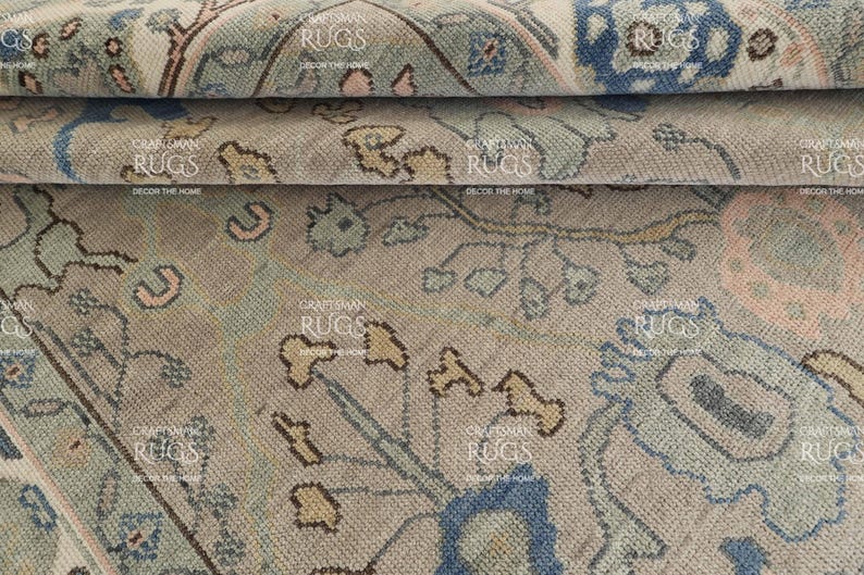 May include: Close-up of a section of a vintage rug with a detailed floral pattern. The rug features a muted colour palette of beige, blue, and pink, with the text "CRAFTSMAN RUGS DECOR THE HOME" visible.