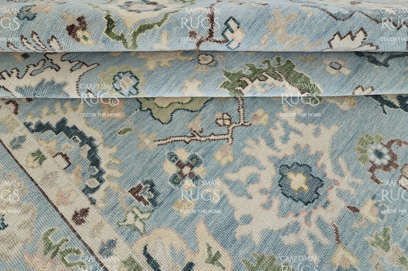 Pu&ograve; includere: Primo piano di un tappeto azzurro con un intricato motivo floreale. Il tappeto presenta una combinazione di tonalit&agrave; blu, beige, verdi e marroni. Il design include fiori stilizzati e forme geometriche.
