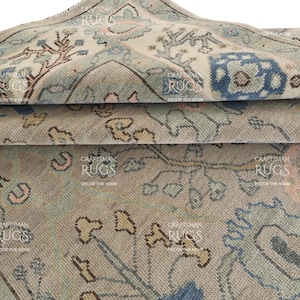 May include: Close-up of a rolled-up area rug with a faded, vintage look. The rug features a complex pattern in shades of beige, blue, and brown. The design includes floral and geometric elements, creating a traditional aesthetic. The rug is made of a soft, woven material.