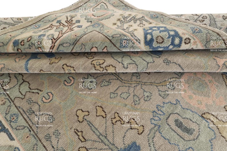 May include: Close-up of a rolled-up area rug with a faded, vintage appearance. The rug displays a complex pattern in beige, blue, and brown hues. The design incorporates floral and geometric elements, creating a traditional aesthetic. The rug is made of a soft, woven material.