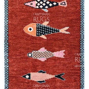 Könnte beinhalten: Ein rechteckiger, roter Teppich mit einem sich wiederholenden Muster aus stilisierten Fischen in Rosa, Orange, Schwarz und Weiß. Der Teppich hat einen blau-weißen Rand. Der Text "CRAFTSMAN RUGS" ist sichtbar.