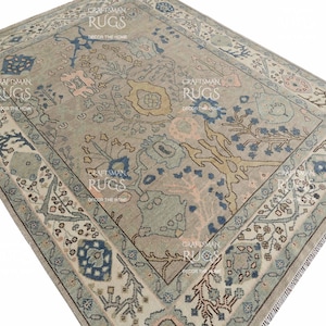 May include: A rectangular rug with a central floral pattern in beige, blue, and pink hues. The rug has a detailed border with geometric and floral designs. The text "CRAFTSMAN RUGS DECOR THE HOME" is visible on the rug.