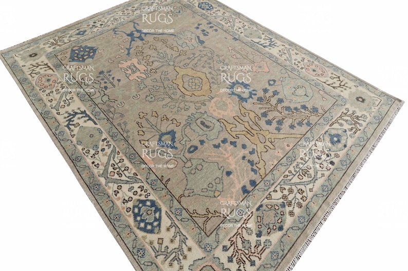 May include: A rectangular rug with a central floral pattern in beige, blue, and pink hues. The rug has a detailed border with geometric and floral designs. The text "CRAFTSMAN RUGS DECOR THE HOME" is visible on the rug.